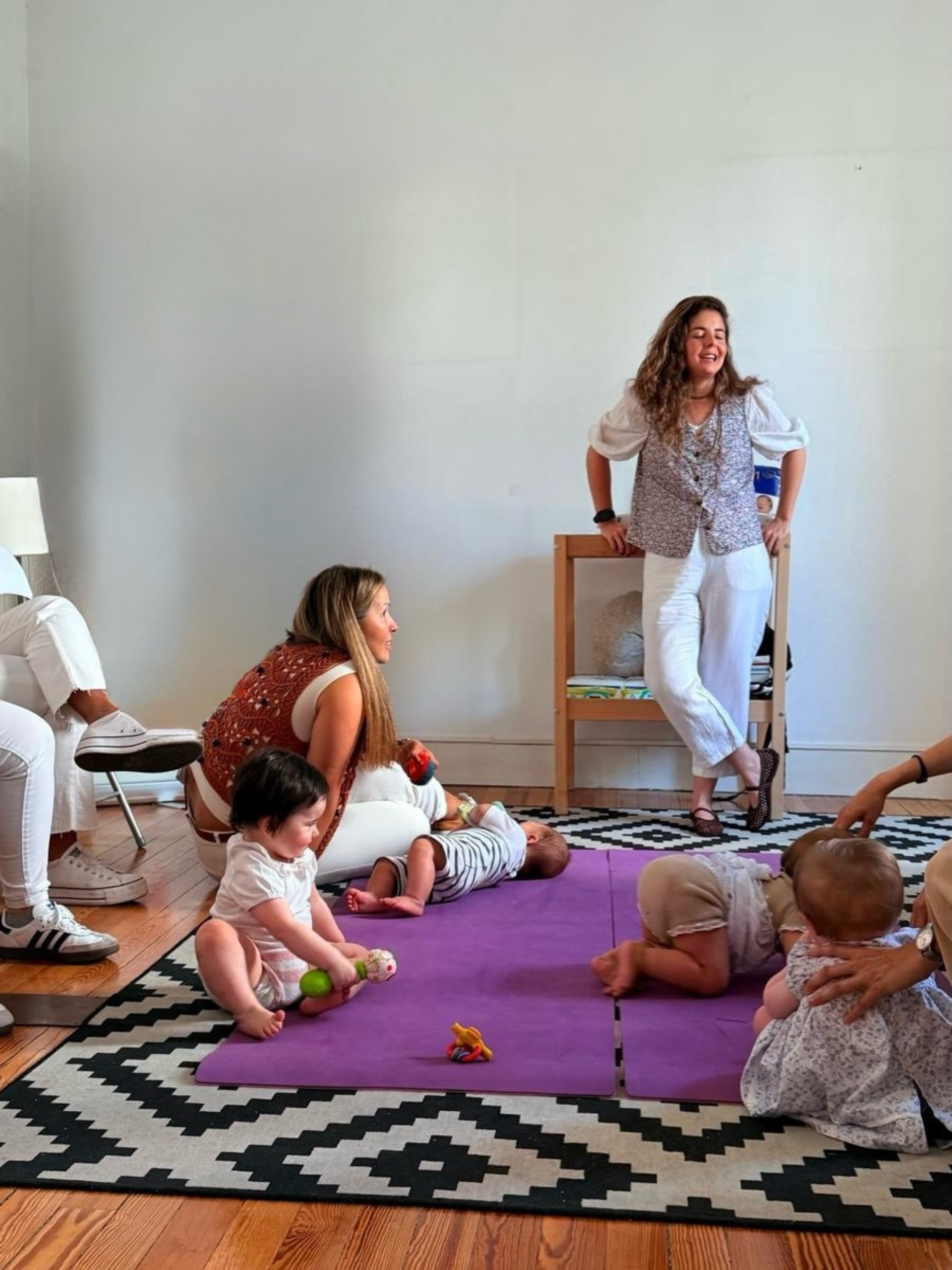 Grupo de madres con sus bebés sobre esterillas moradas mientras la matrona Elena Tovar Muñoz dirige el curso en una sala luminosa.