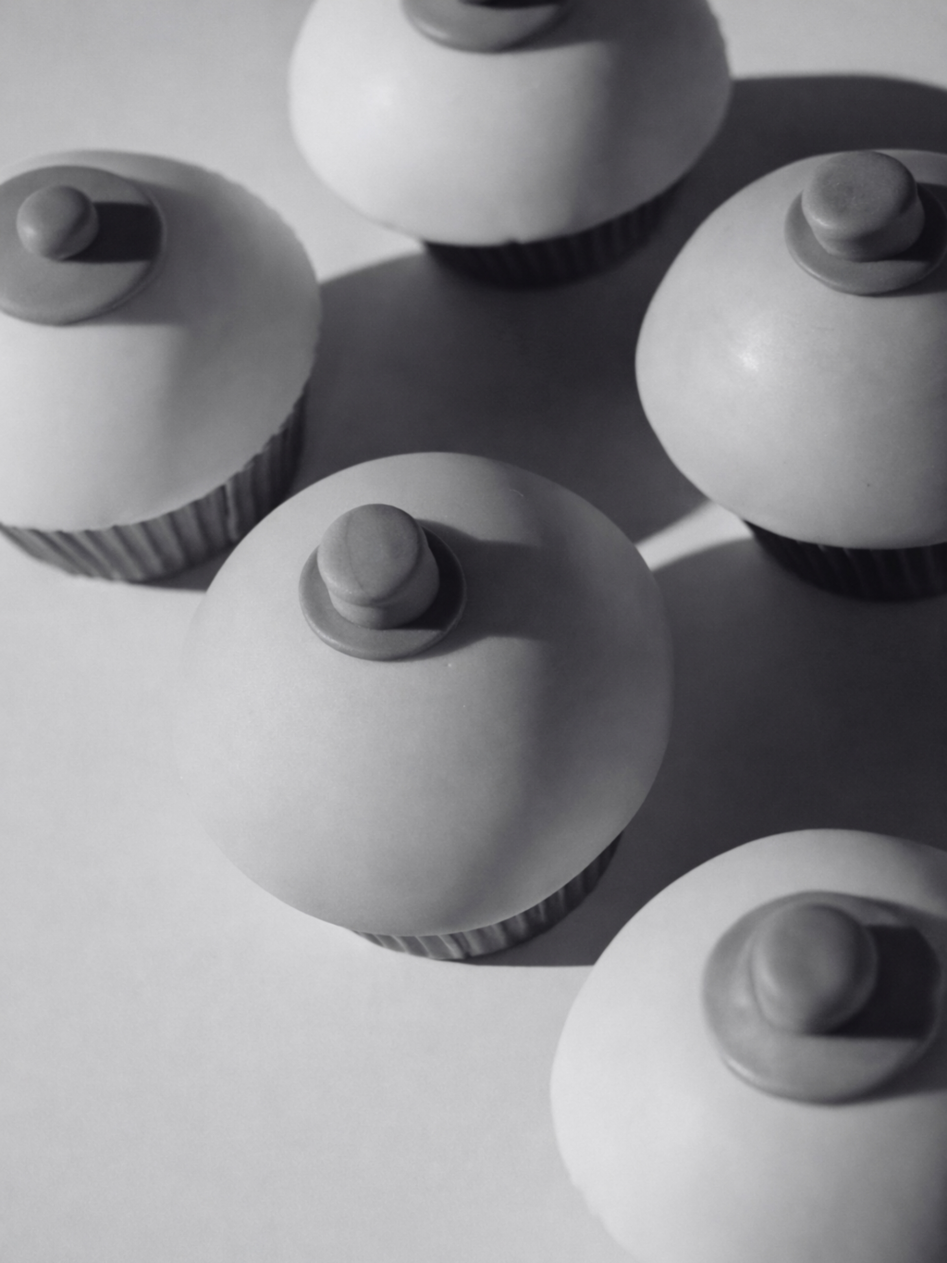 Cupcakes decorados con glaseado que simula un pecho con pezón, vistos desde arriba en blanco y negro.